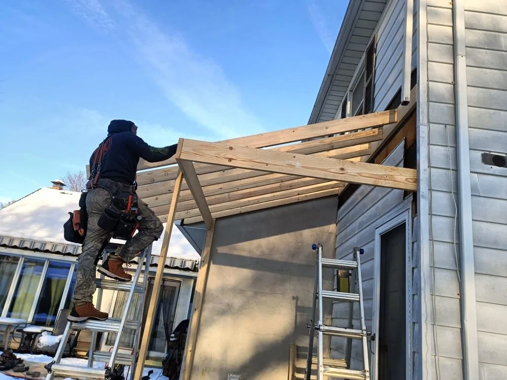 A worker on a ladder fixing the top plate of a lean-to roof frame in winter