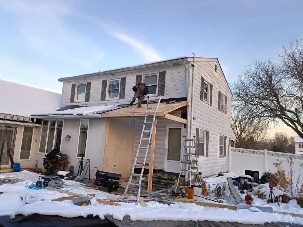 A low addition roof framed against a taller two storey wall with snow lying on both roof planes